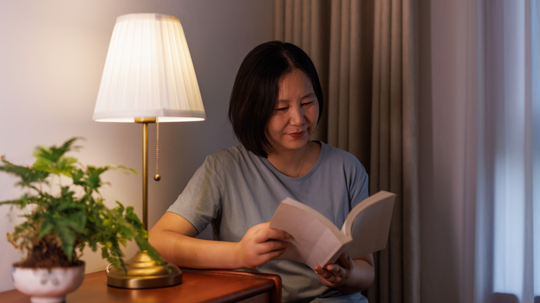 Woman reading a book in a corner with a table lamp