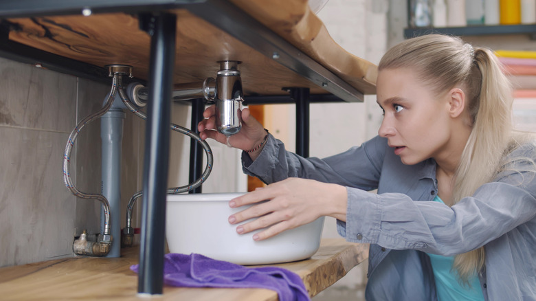 woman putting bucket under a sink