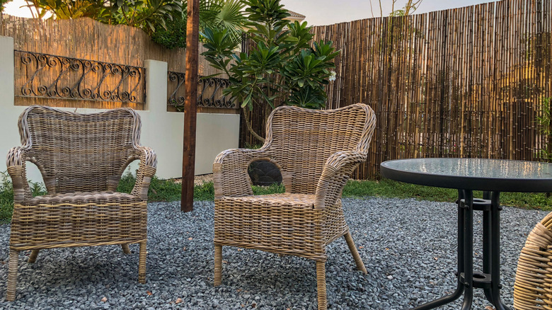 Backyard seating area with gravel, a willow fence, and wicker chairs.