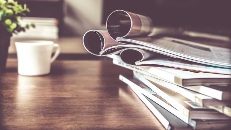 A stack of magazines by a coffee cup