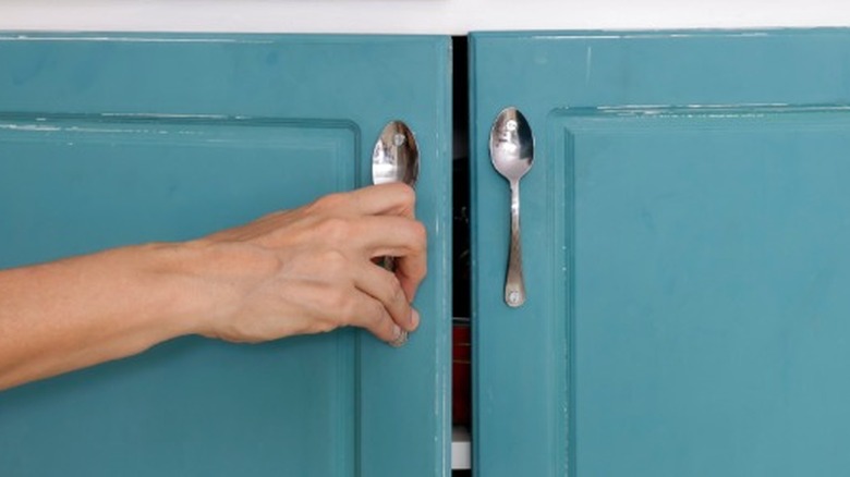 A person opening up a door with spoons used as the handle.