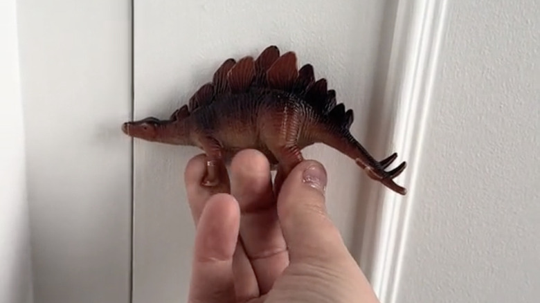 A hand pulling on a dinosaur figure closet door handle.