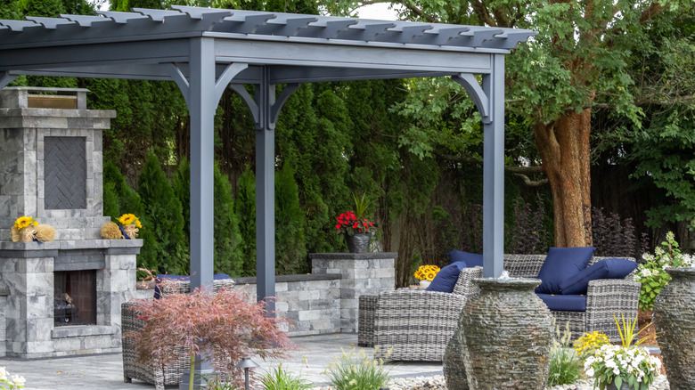 Gray pergola with an outdoor fireplace and lounge chairs