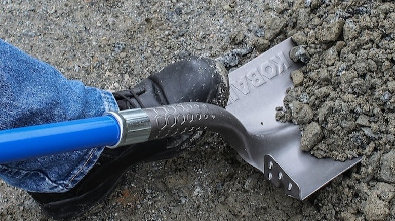 A person digs dirt using a Kobalt digging shovel.