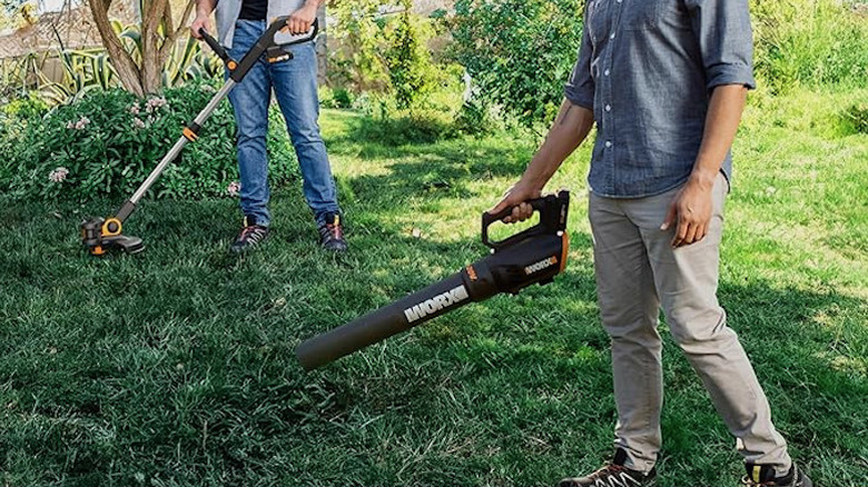 Two men using a leaf blower and trimmer in their backyard.