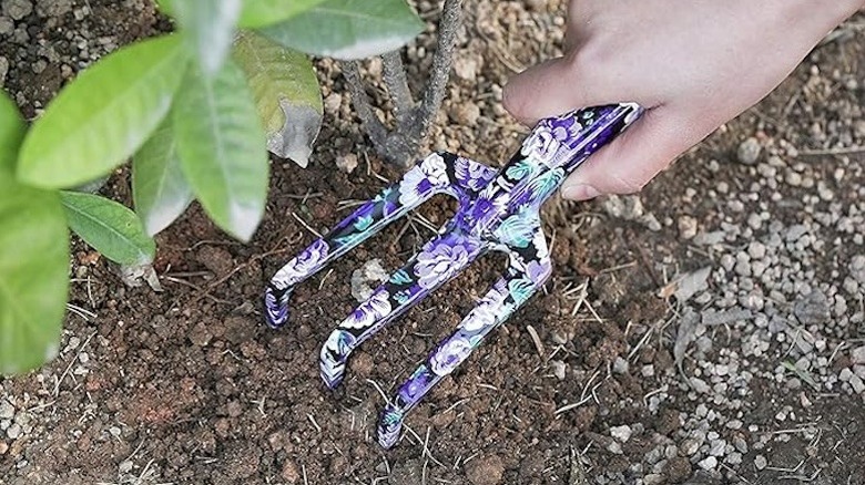 A person uses a cute floral patterned fork tool in the garden.