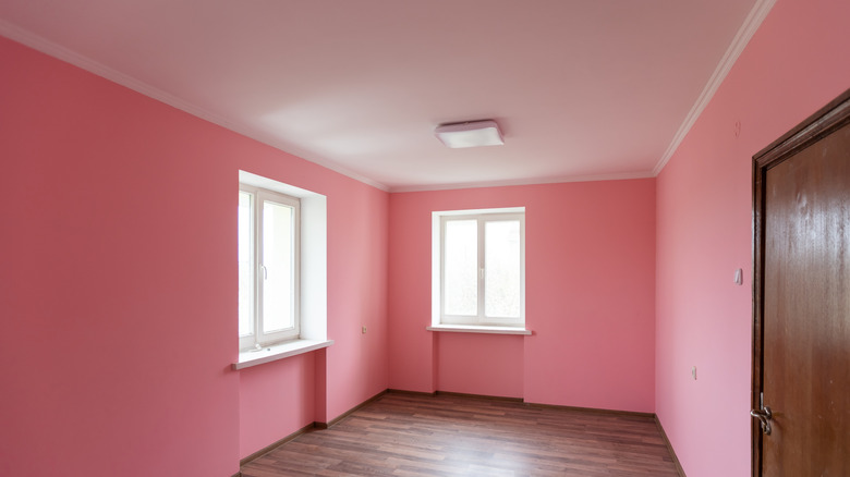 An empty room with wooden floors, a wooden door, and pink painted walls.