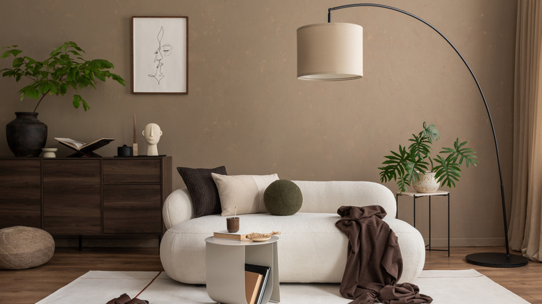 A room with brown painted walls, a white modern couch, and dark brown furniture pieces.