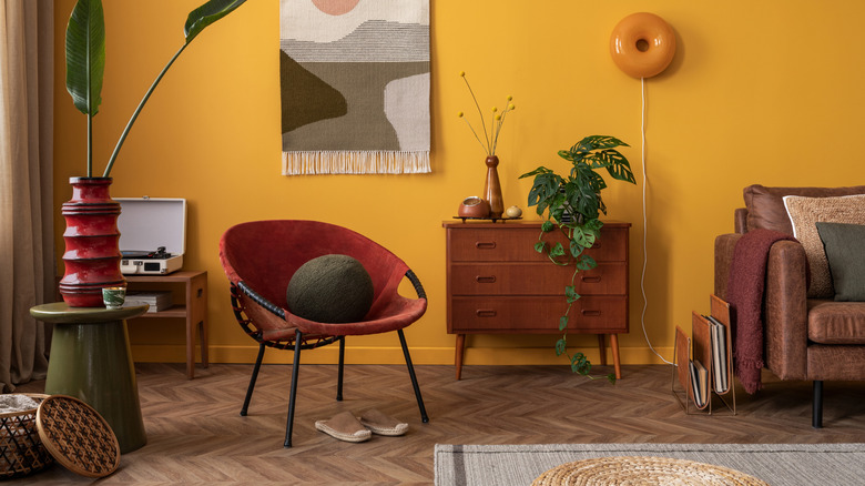 A living with yellow painted walls and brown, red, and green pieces of furniture on herringbone wooden floors.