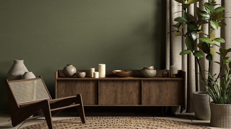 An olive green painted wall with brown furniture pieces and a plant sitting in front of it.