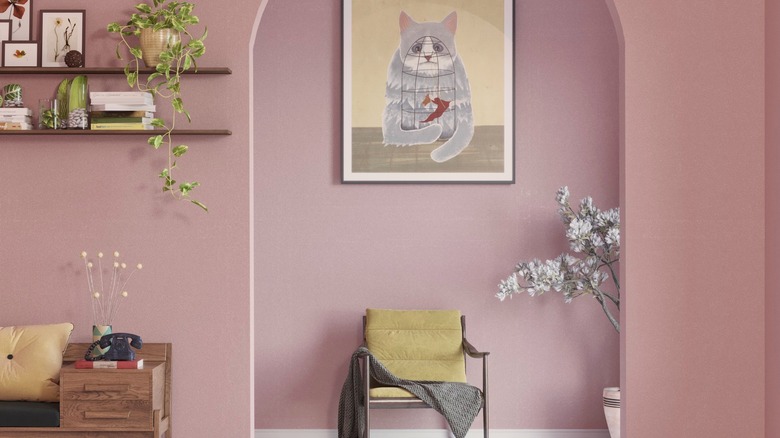 A front hall with a curvey entry into another room, painted in dusty rose pink and furnished with wooden furniture and shelves.