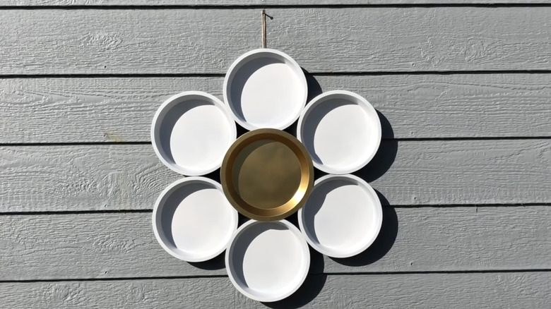 Wall-hung garden art that looks like a daisy and is made from pie tins.