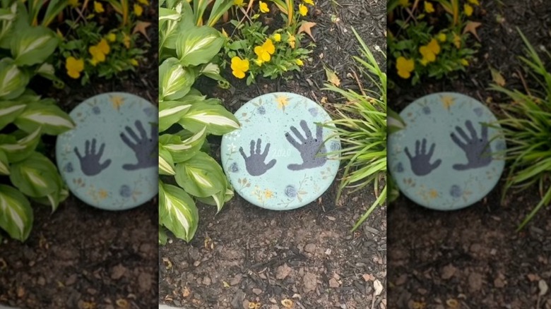 A concrete garden stone made in a pie tin mold decorated with kid's handprints and flowers.