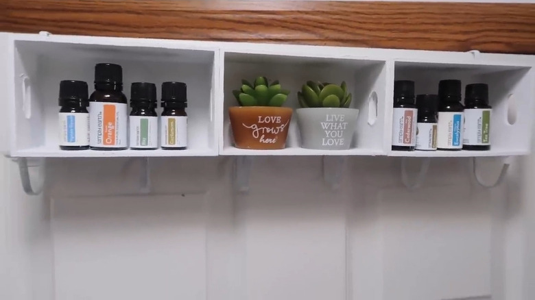 Wood shelves with hanging hooks underneath, two of shelves filled with essential oils