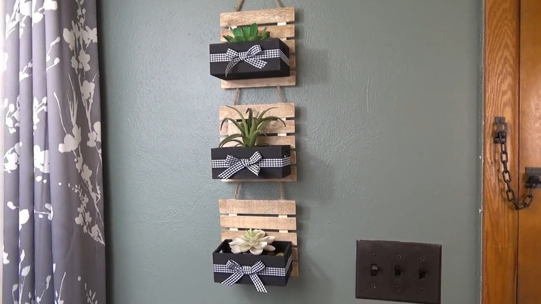 Wood crate and pallet wall planter hung on wall next to purple and white flowered curtain