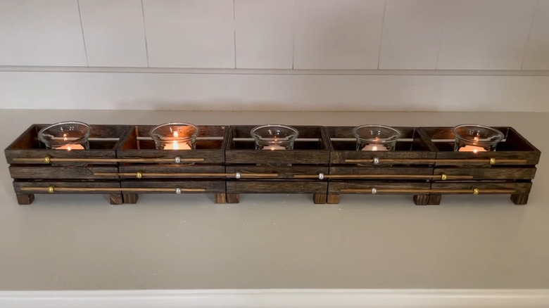 Wooden crate candle holder holds several lit candles on a countertop