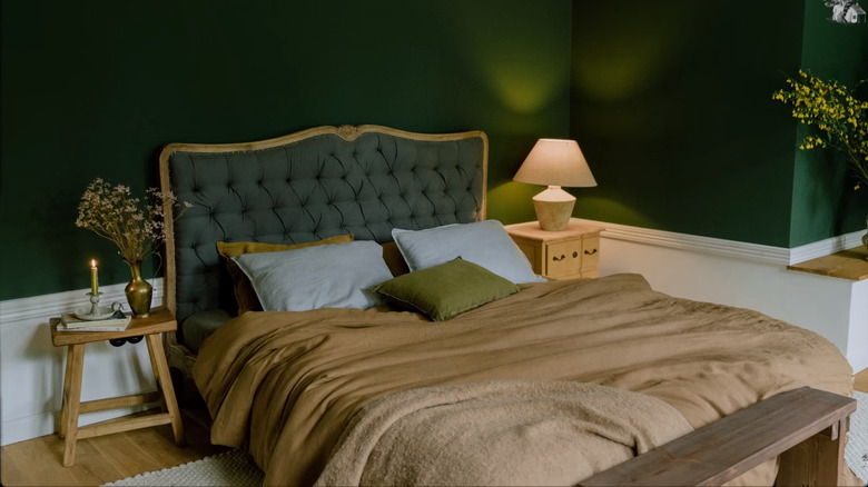 Dark green bedroom with brown covers, gilt headboard, brass, and wood