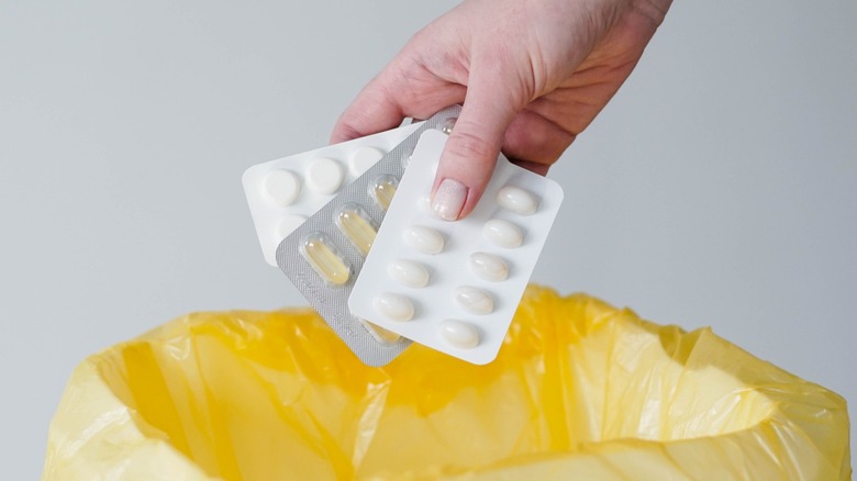 Hand holding pills over trashcan