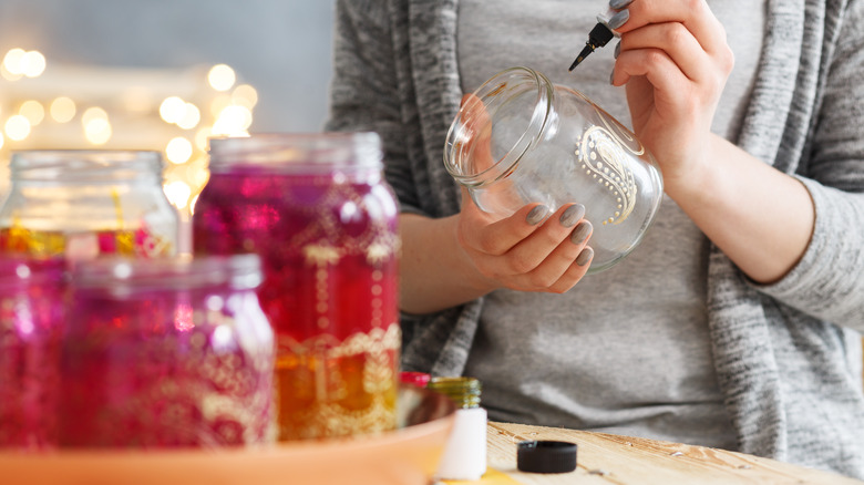 A person decorating mason jar centerpieces with paint.