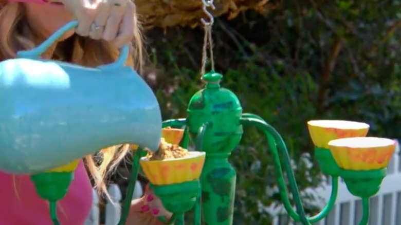 Woman pouring bird seed into bowls in upcycled chandelier feeder