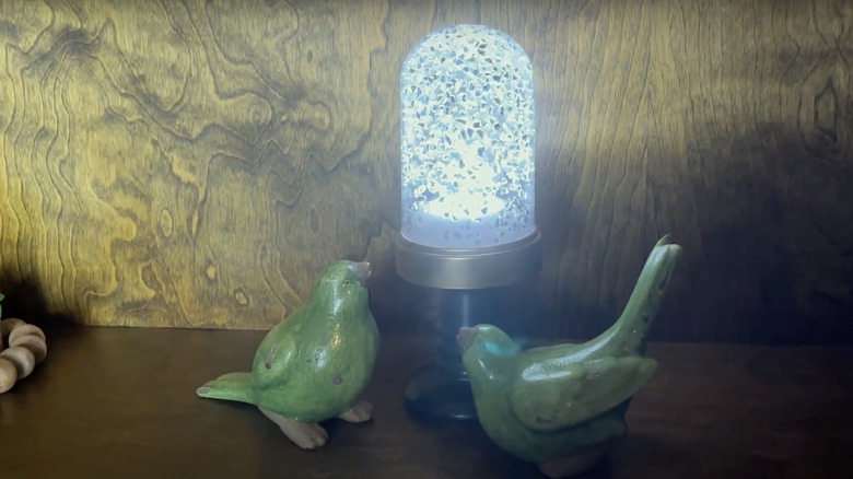The DIY project sits on a shelf next to two green birds