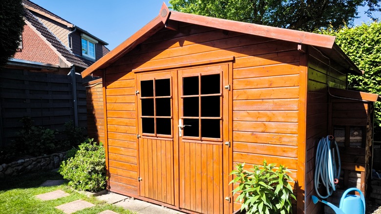 A wooden garden shed sits in a backyard