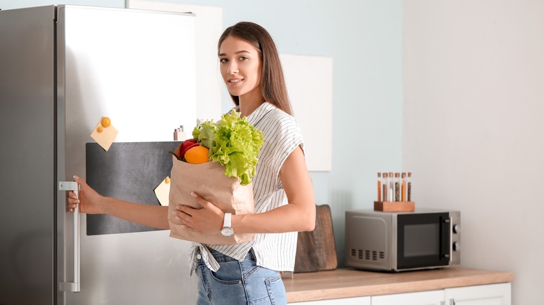 Woman stocking fridge with fresh produce