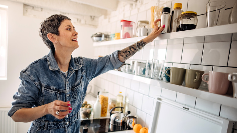 Woman putting flask up on kitchen shelf