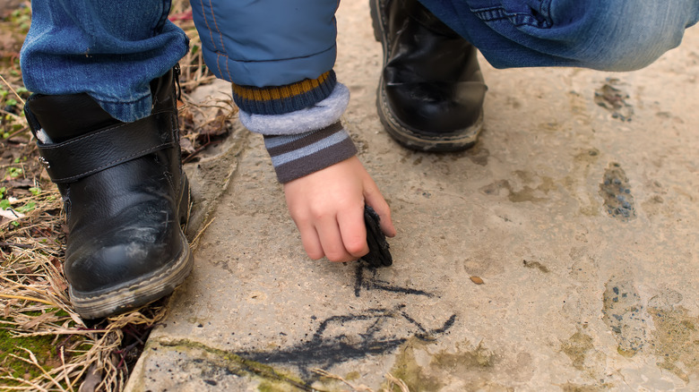 child drawing on sidewalk with charcoal