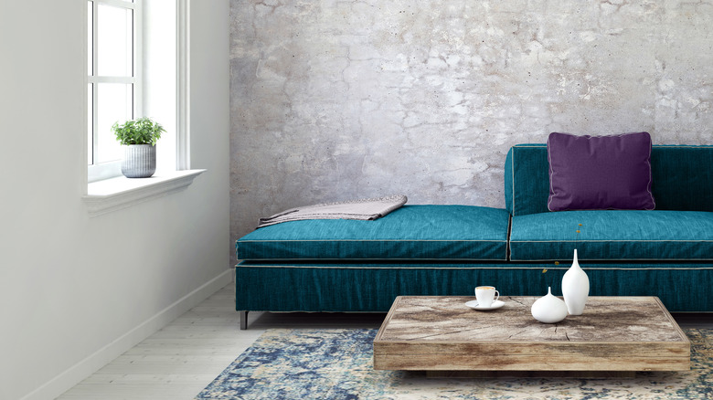 Corner of a living room with blue sofa and gray cement accent wall