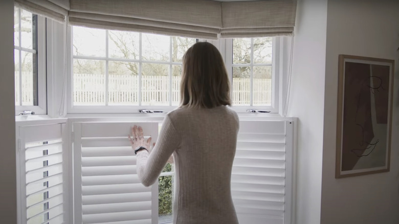 A woman closes cafe shutters fitted across a bay window