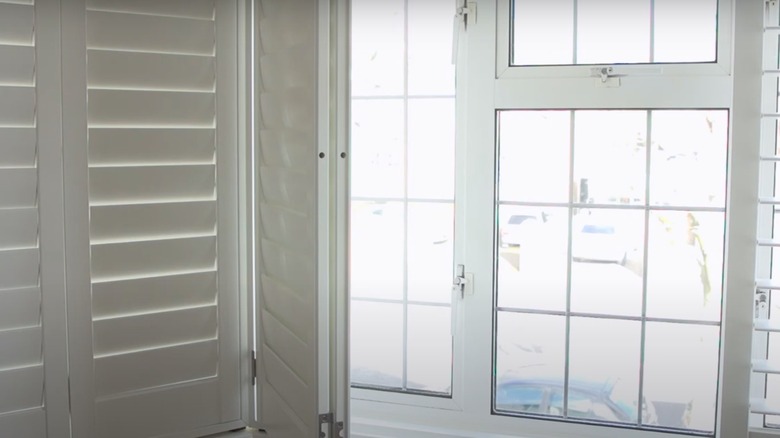 White full-length shutters in a bay window bedroom