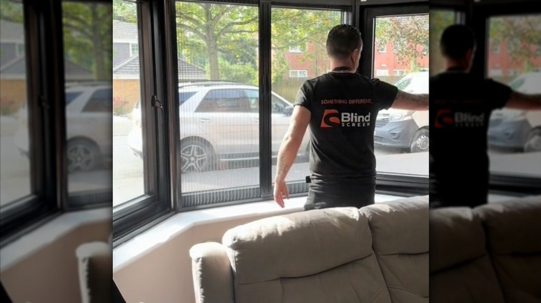 A sales representative demonstrates opening and closing fly screens mounted to a bay window