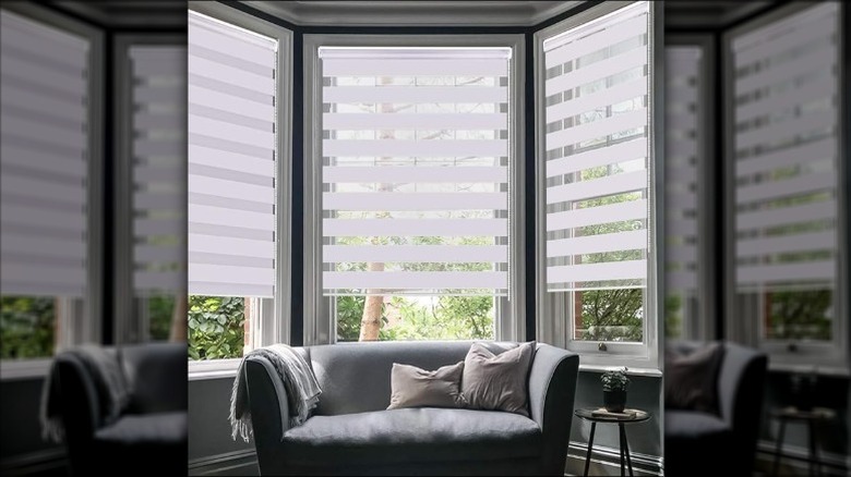 A residential bay window dressed with white striped roller blinds