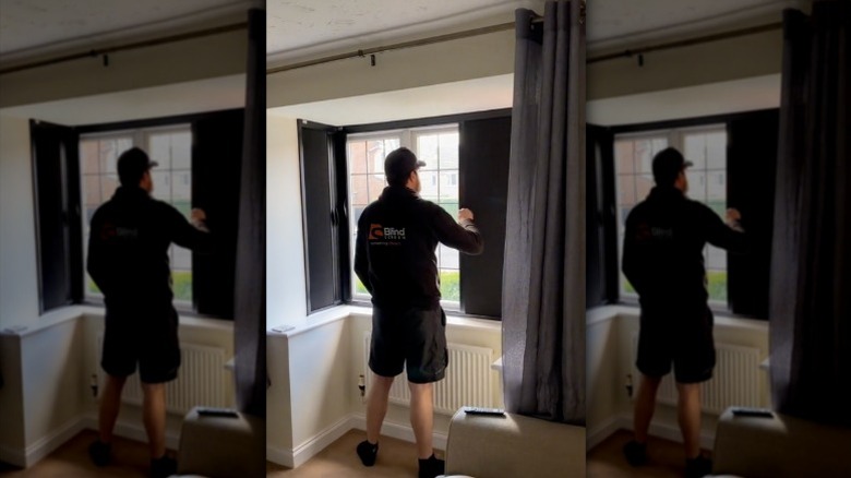 A shade installer demonstrates how to close blackout blinds on a bay window