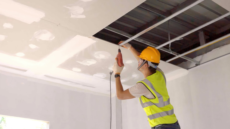 A professional attaching drywall to the ceiling of a home