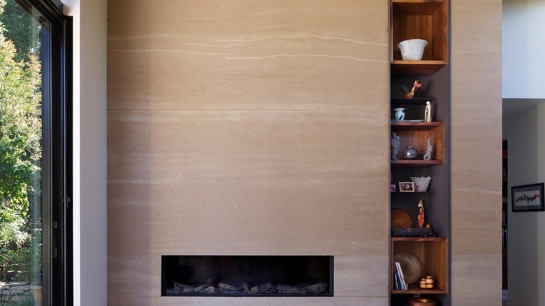 Rammed earth wall with fireplace and open shelves in house