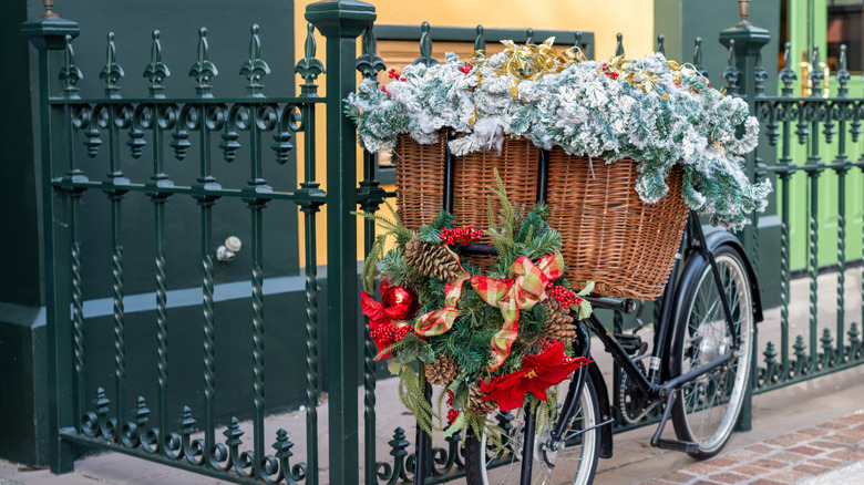 Bicycle locked to iron fence, holding basket full of evergreens and bows