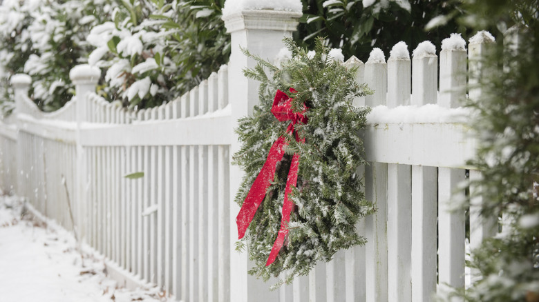 Green wreath with a red bow on white fence