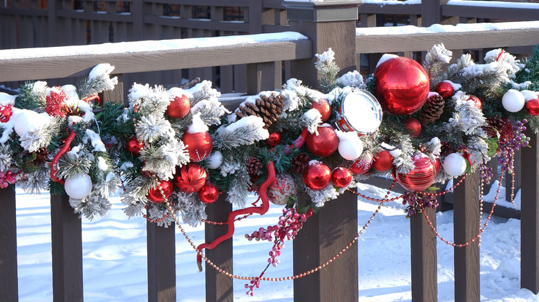 Christmas garland with pine cones, ornaments, beaded strings, and evergreen twigs on a fence