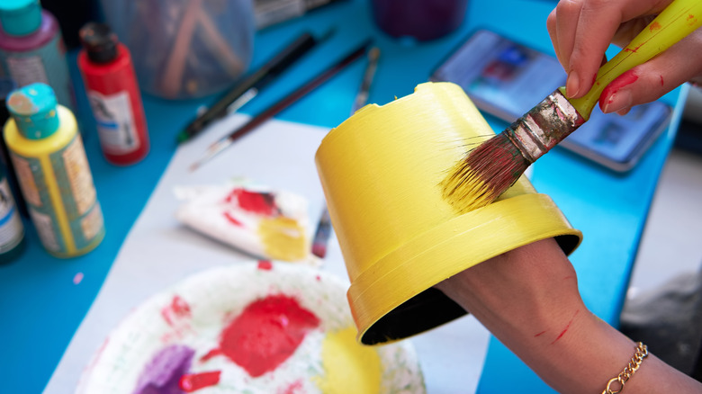 A person painting a yellow plastic pot above craft table