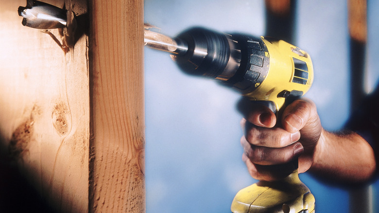 Worker drilling through wood with a black and yellow power drill