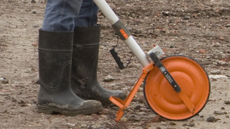 Worker will black gumboots holding a measuring wheel