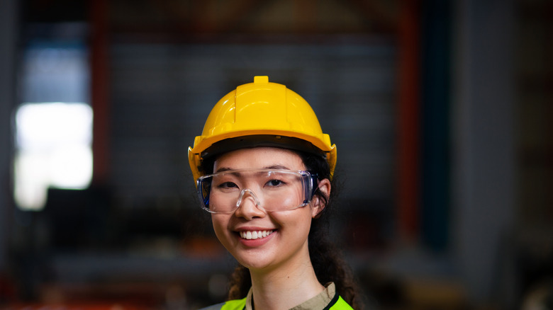 A woman with a yellow hard hat and safety glasses smiling