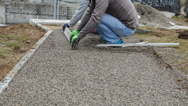 Worker leveling a metal screed board on gravel