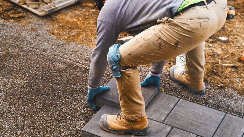 A man with blue knee pads and gloves laying pavers