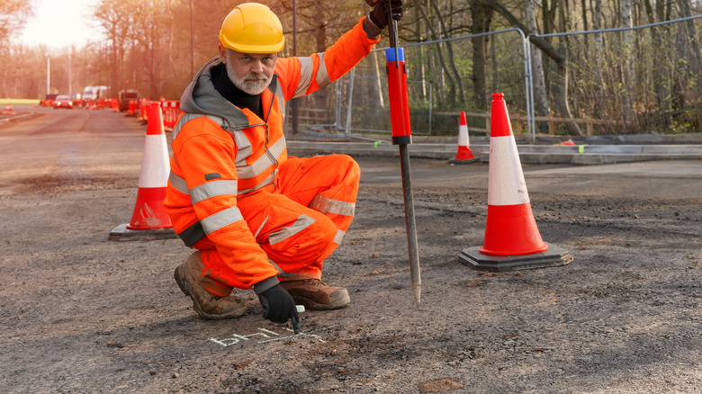 Construction worker in orange gear marking the ground with chalk