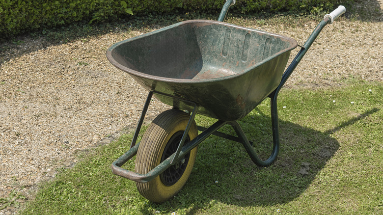 A wheelbarrow on green grass next to a mixture of soil and gravel