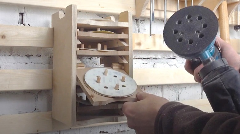 man holding orbital sander while pulling out sander pad shelf on French cleat sander storage rack