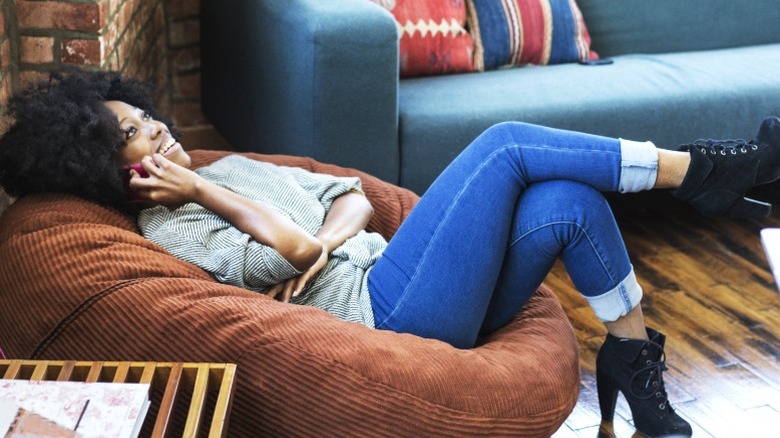 Smiling woman on cell phone relaxing in brown beanbag chair in industrial loft apartment